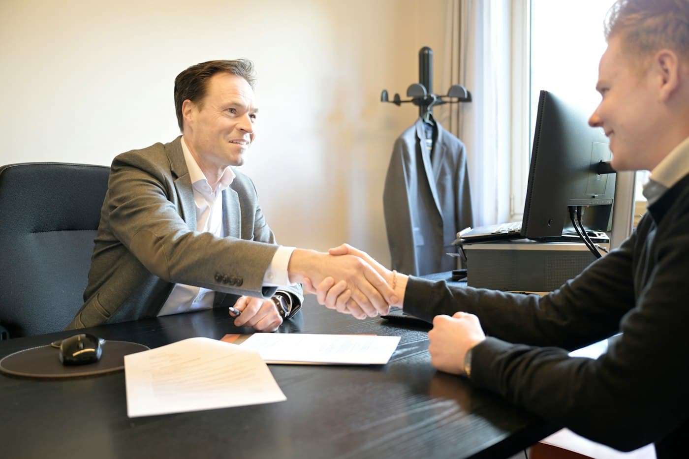 Two business partners shaking hands across an office desk